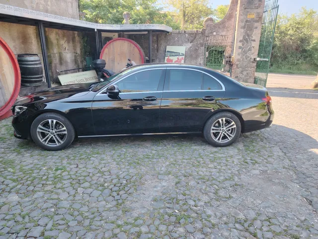 La Mercedes Classe E nera di Luxury Travel Agency vista di profilo, davanti a una cantina